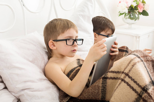 Deux garçons jouent à l'ordinateur portable et tablette avec chien au lit
 - Photo, image