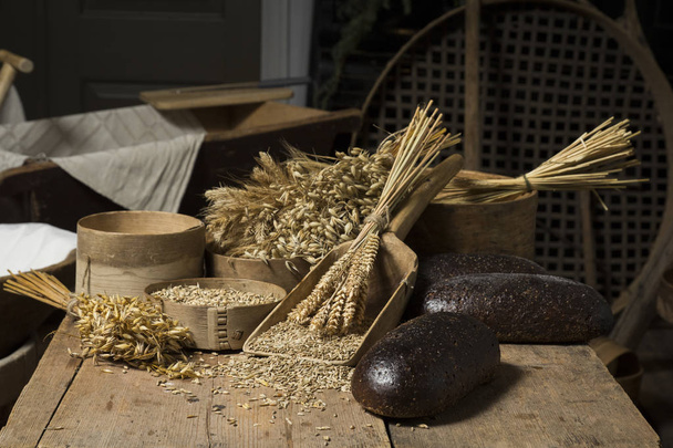 Fondo de pan. Composición de panes integrales marrones sobre madera rústica con espigas de trigo esparcidas
 - Foto, Imagen