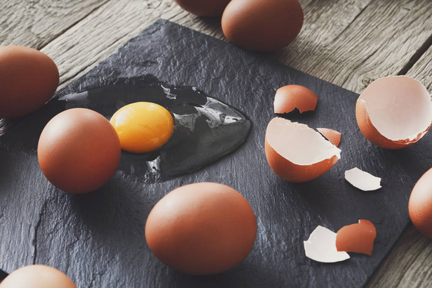 Brown organic cracked eggs with yolk on black background - 写真・画像