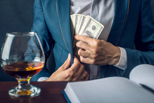 Man Businessman in suit puts money in his pocket. A bribe in the form of dollar bills. Concept of corruption and bribery - Photo, image