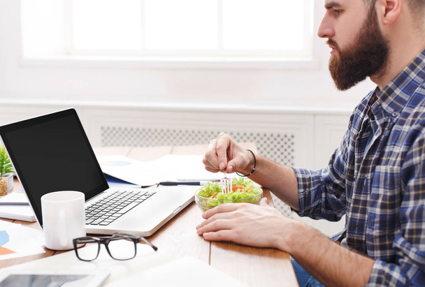 Člověk má zdravé pracovní oběd v moderních kancelářských interiérů. Mladý pohledný podnikatel na pracoviště s zeleninový salát mísy, diety a jíst správné koncepci. - Fotografie, Obrázek