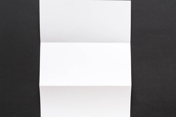 Wit gevouwen vel papier op zwarte achtergrond - Foto, afbeelding