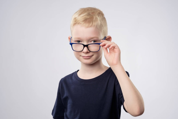 Ładny blond chłopiec kaukaski trzyma okulary w pobliżu oczy - Zdjęcie, obraz