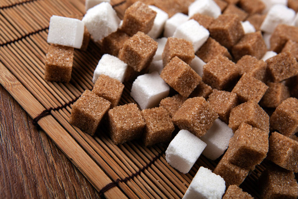 кубики белого и коричневого сахара на бамбуковой салфетке
 - Фото, изображение