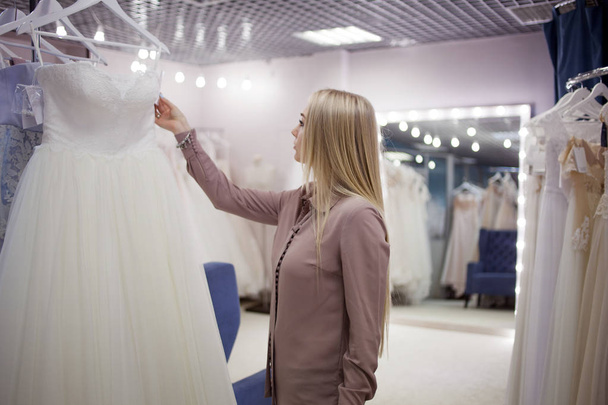 Beautiful girl chooses her wedding dress. Young woman entrepreneur. Portrait in Bridal salon - Fotografie, Obrázek