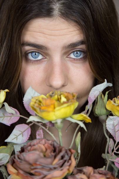 Portrait d'une belle jeune fille blanche aux yeux bleus et aux cheveux bruns tenant un bouquet de fleurs séchées. Elle a un regard sérieux et un peu triste
.  - Photo, image