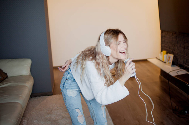 Young pretty girl in headphones with the phone. Listening to music, dancing and singing, indoors - Photo, Image