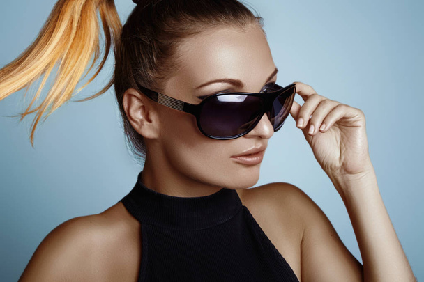 Beautiful young woman with black fashion sunglasses and glamour pinytail hairstyle. Eye wear style - 写真・画像