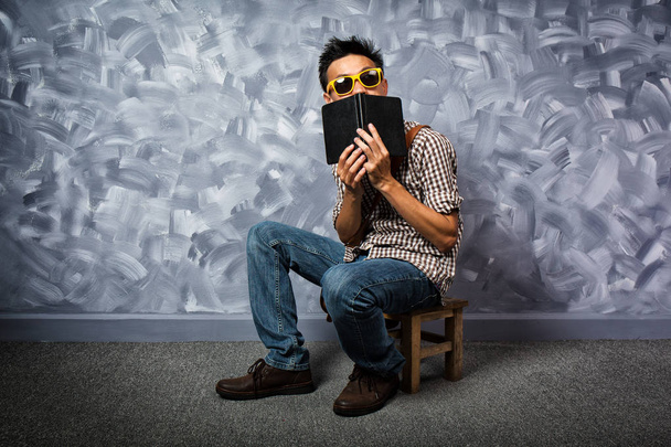 Χίπικο στυλ Ασιάτης/ισσα άνθρωπος με βιβλίο σε vintage σοφίτα τοίχου τσιμεντένιο στιλ δωμάτιο. - Φωτογραφία, εικόνα