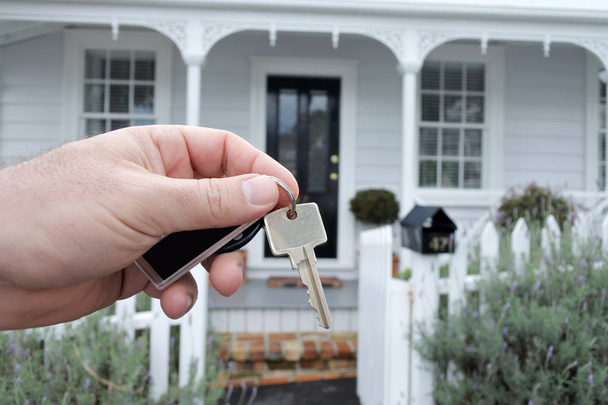 Ένα επανδρώνει χέρι κρατά ένα κλειδί ενάντια σε ένα σπίτι στο Auckland της Νέας Ζηλανδίας - Φωτογραφία, εικόνα