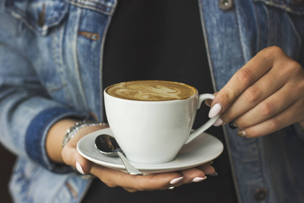 The young woman in jeans jacket holding the cup of coffee in her hands - Foto, Imagem