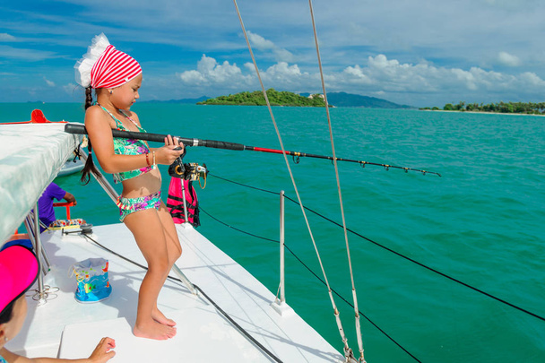 Ένα κορίτσι είναι η αλιεία σε μια βάρκα. Πολύχρωμο τροπικό μοτίβο γύρω από - Φωτογραφία, εικόνα
