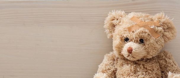 Медвежонок с повязкой на деревянном полу
 - Фото, изображение