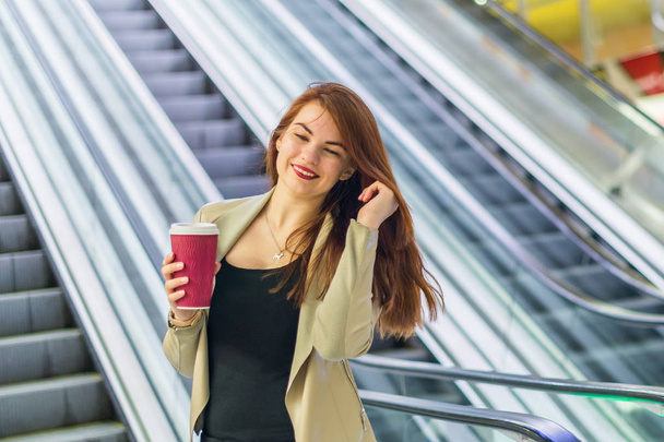 The girl smiling and holding mug of coffee near escalator at the subway - Foto, Imagem