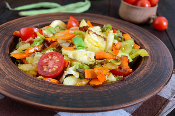 Vegetable stew of cabbage, green beans, carrots, tomatoes, onions, sweet peppers in a clay bowl on a dark wooden background. - Photo, Image