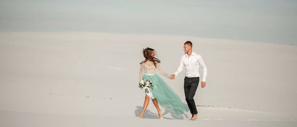 Наречений і наречений тримають руки, посміхаються і ходять босоніж в пустелі. Вільямс
 - Фото, зображення