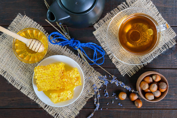 Uma xícara de chá de ervas, mel, favo de mel, avelãs em um fundo de madeira escura
.  - Foto, Imagem
