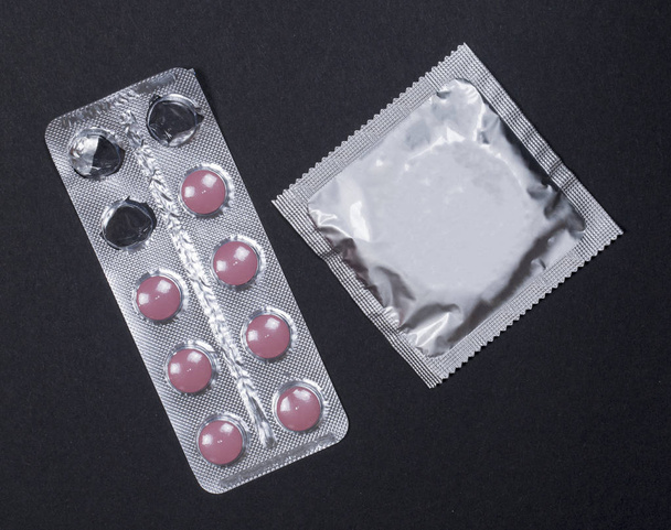 Презерватив і таблетки контролю за народжуваністю контрацепції, вагітність захисту на чорному фоні. - Фото, зображення