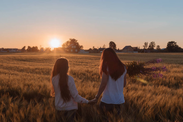 Mom and daughter hold hands and step on the yellow field. - Φωτογραφία, εικόνα