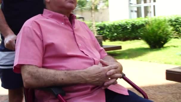 syn spacery z niepełnosprawnym ojcem na wózku inwalidzkim w parku - Materiał filmowy, wideo