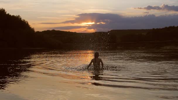 tyttö auringonlaskun aikaan leikkii vedessä, tyttö kädet roiskuu vettä, hidastettuna
 - Materiaali, video