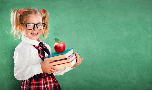Pequeña colegiala sosteniendo libros y manzana
 - Foto, imagen