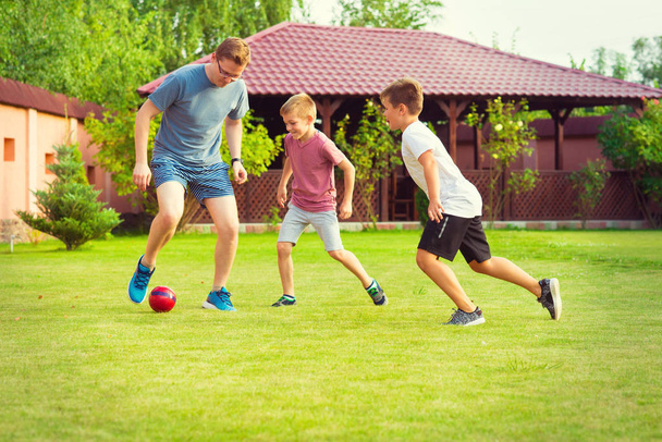Dwaj synowie szczęśliwy gry w piłkę nożną z ojcem w ogrodzie w pobliżu - Zdjęcie, obraz