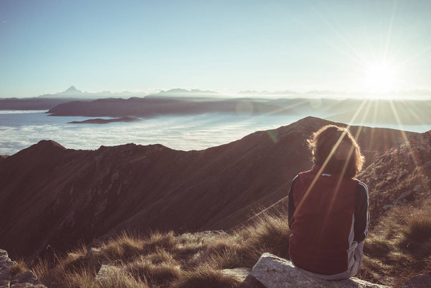 Женщина-туристка достигает своей цели на вершине горы и смотрит на величественный панорамный вид на Альпы с горной вершиной на заднем плане. Широкий угол обзора на закате в подсветке, тонированное изображение, винтаж
 - Фото, изображение