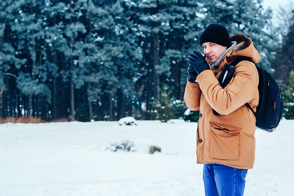 kar üzerinde duran ve bir termos ve bir fincan çay tutan bir sırt çantası ile kırmızı ceketli genç bir adam. Kış orman. - Fotoğraf, Görsel