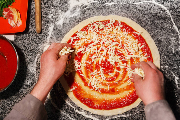 Geraspte kaas toevoegen aan pizza bovenaanzicht - Foto, afbeelding