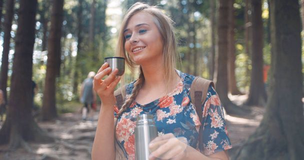 Beautiful blonde girl pouring tea from thermos. - Photo, image