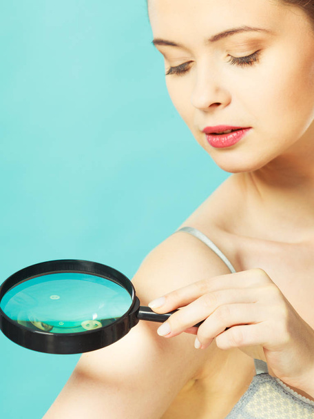 Woman using magnifying glass to examine her moles skin - Zdjęcie, obraz