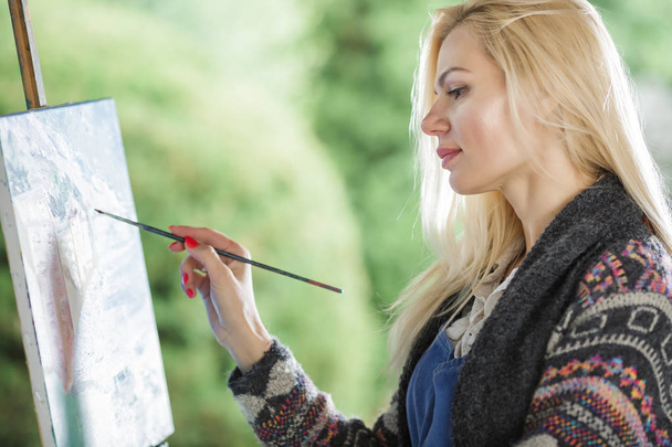 woman artist with a brush in her hand draws on canvas - Φωτογραφία, εικόνα