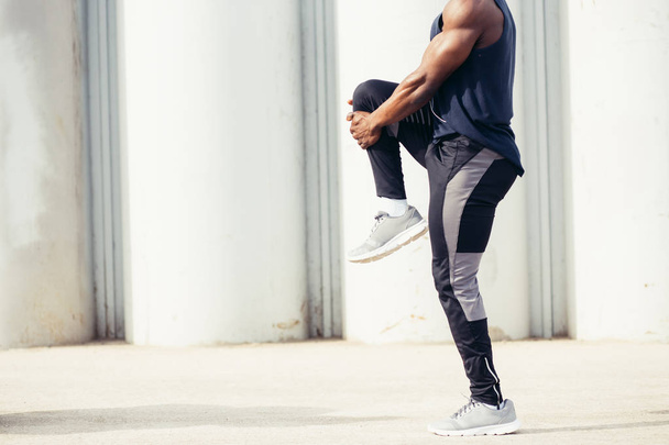 Black man doing stretching before running in urban background. - 写真・画像