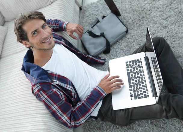 business guy with laptop sitting on carpet in living room. - Фото, изображение