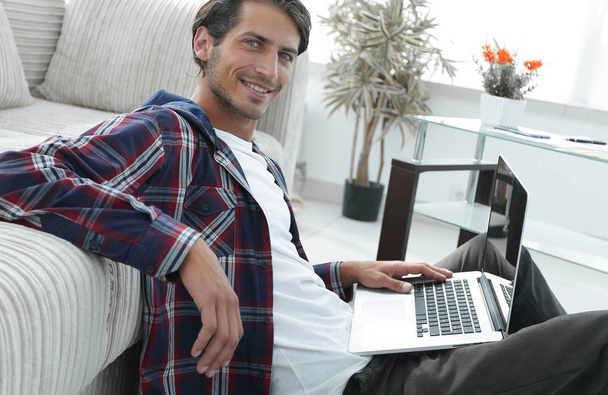 charming young man with laptop sitting in modern living room - Photo, image