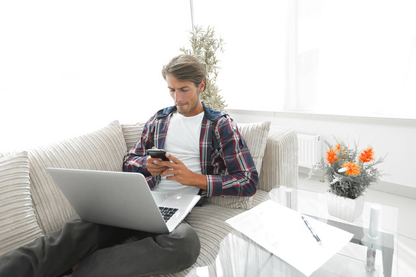 serious young man with laptop and smartphone in living room. - 写真・画像