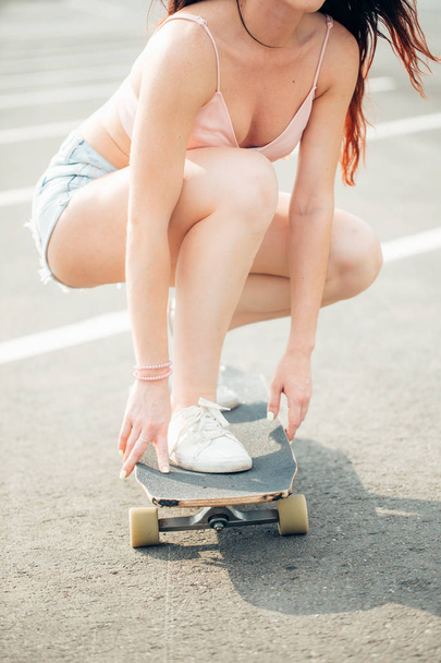 Beautiful young girl sits and ride on longboard in sunny weather - Fotoğraf, Görsel