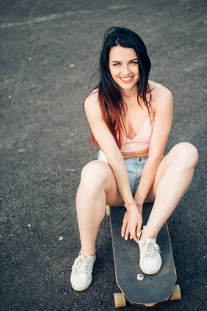Skateboarder girl smiling. Hipster girl sitting on skateboard - Valokuva, kuva
