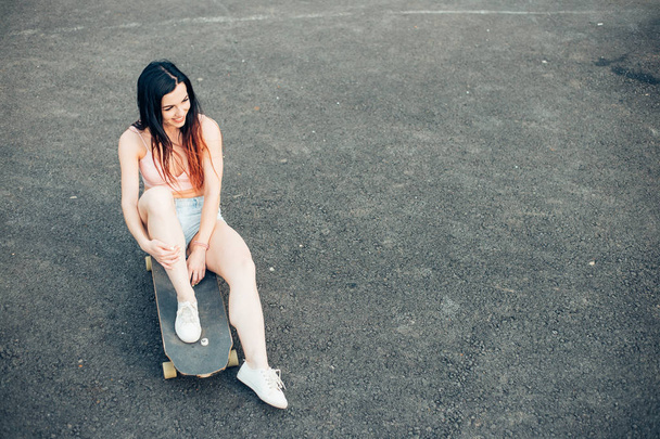Skateboarder girl smiling. Hipster girl sitting on skateboard - Фото, изображение