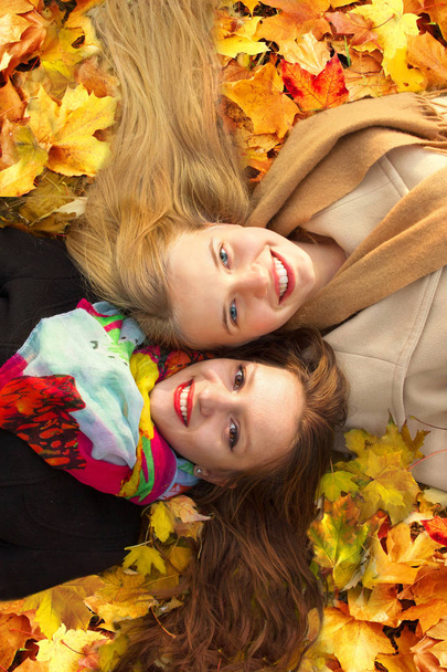 two girls lie on a leaf in an autumn park - Foto, afbeelding