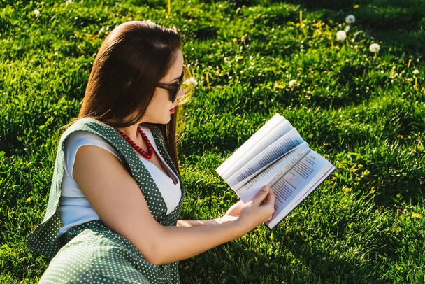 Olvasó nő a fű. Park, napszemüveget hallgatónak készül - Fotó, kép