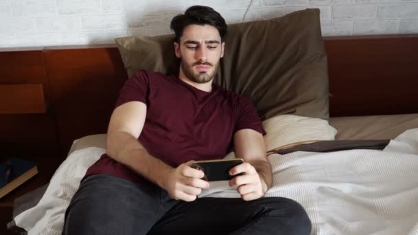 Young man watching movie on cellphone in bed - Filmagem, Vídeo