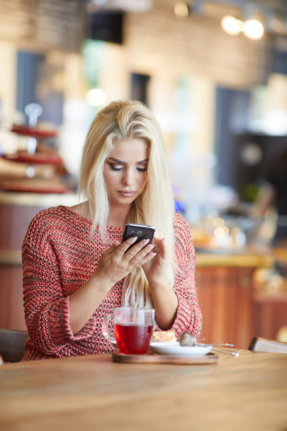 γυναίκα ή επιτυχημένη εργασία στο smart phone στο καφενείο εσωτερικό, θηλυκό μαθητή να κάθεται στην βιβλιοθήκη του Πανεπιστημίου ενώ χρησιμοποιώντας τεχνολογία, Διαδίκτυο εργασία εξ αποστάσεως - Φωτογραφία, εικόνα