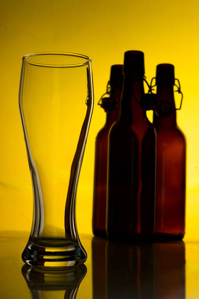 Empty beer glass with beer bottles on color background - Photo, image