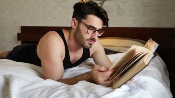 Young man lying in bed and reading a book - Video, Çekim