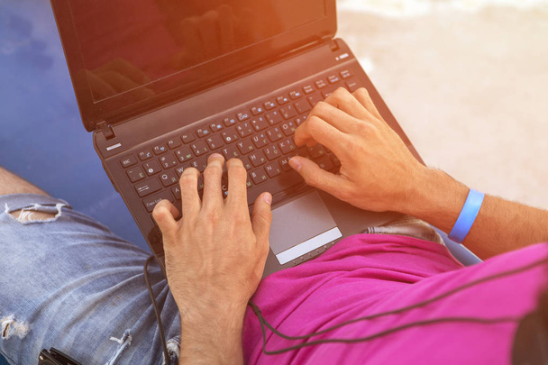 Man working on a laptop remotely, typing, sitting on a tropical  - Φωτογραφία, εικόνα