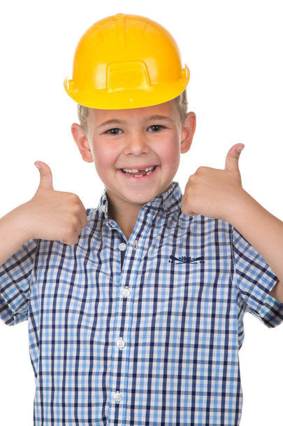 Smiling handsome caucasian teen boy in a yellow hard hat. Happy child making thumbs up gesture and looking at camera. - Foto, afbeelding