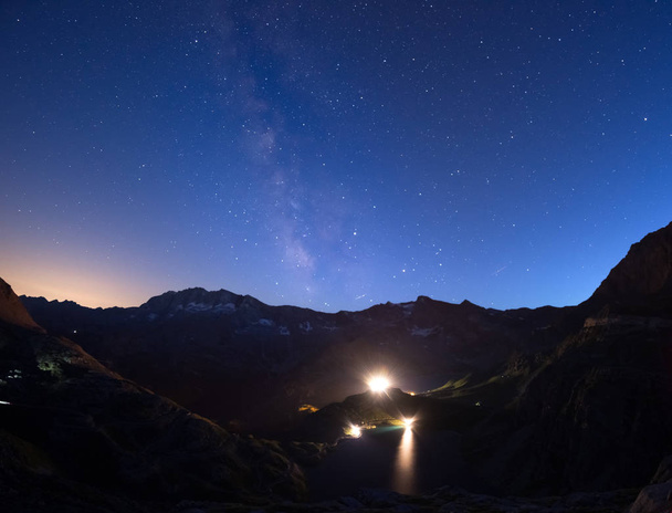 The colorful glowing Milky Way arch and the starry sky from high up on the Alps. Lights from hydroelectric lake dam. - Fotó, kép