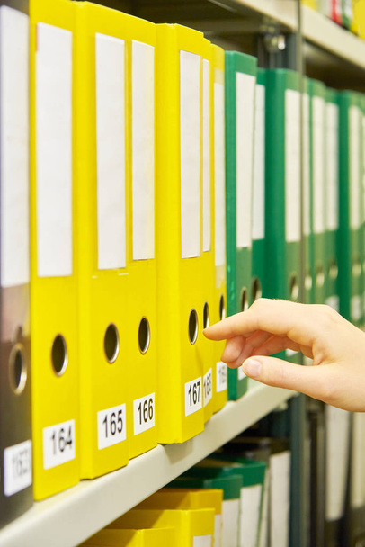 Yellow, green and black file folders in archive and human hand selecting one of them - Photo, Image